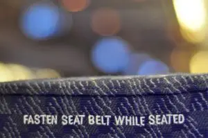 'Fasten seat belt while seated' embroidered on the back of an airline chair. The image shows that while embroidered text is legible, the letters are uneven.